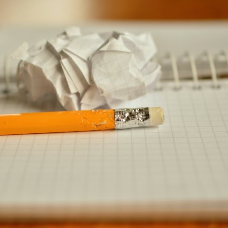 Open notebook with a balled up scrap of paper and pencil with the end slightly chewed showing writing frustration
